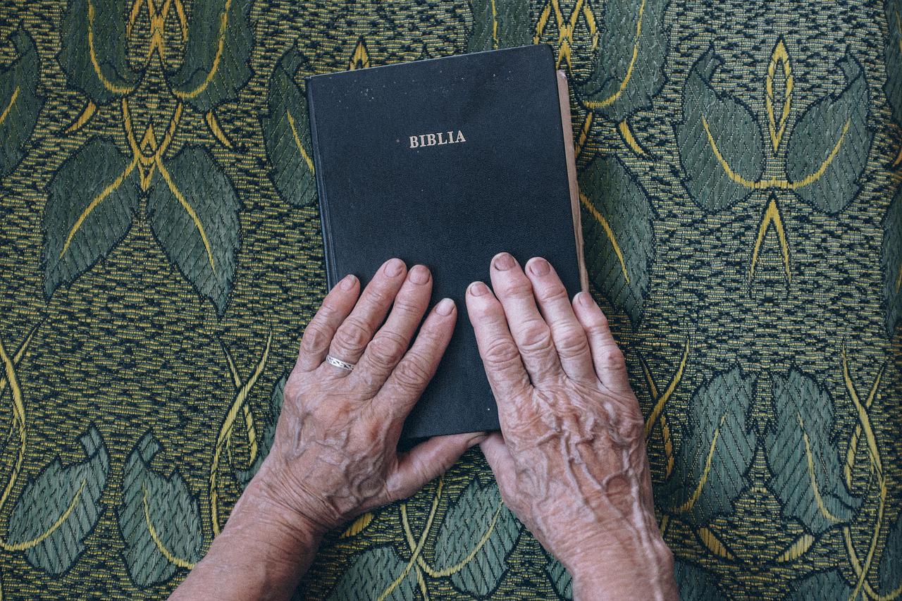 Dwie dłonie starszego człowieka położone na Piśmie Świętym