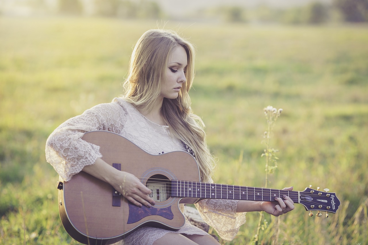 Kobieta grająca na gitarze siedząca na łące